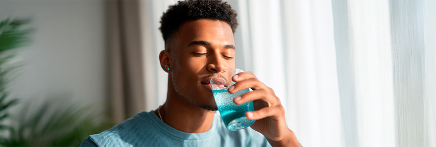 Young man drinking clear blue water, taking care of health, healthy lifestyle and well-being