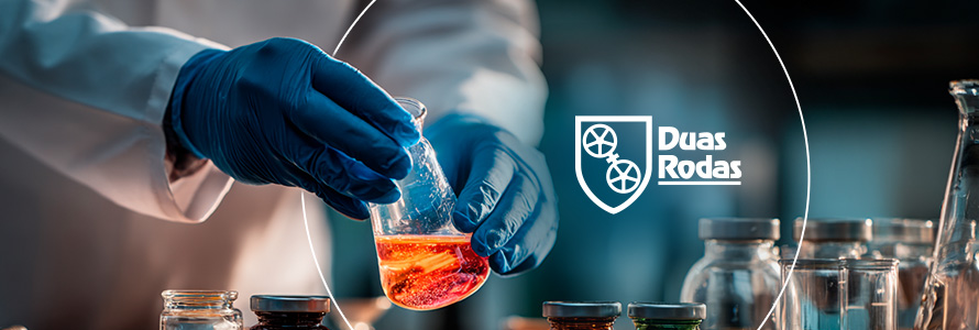 A researcher in a laboratory manipulating a sample of orange liquid in a test cylinder, with several vials around it, representing science and innovation in the laboratory.