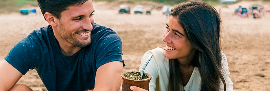 Feliz pareja en la playa bebiendo mate.