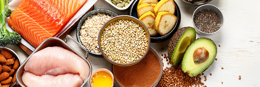 Mesa com alimentos ricos em proteínas e fibras, como salmão, aveia, abacate e frango.
