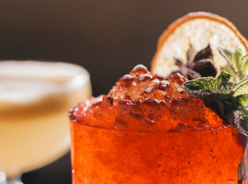 Frosty red cocktail with mint and star anise beside creamy cocktail