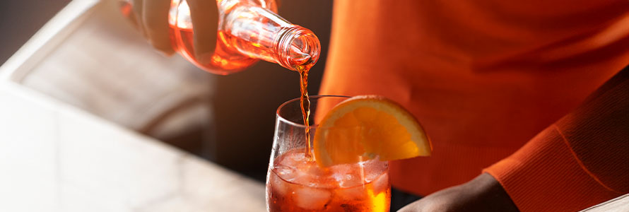 Bartender servindo um drink laranja em copo com gelo e fatia de laranja