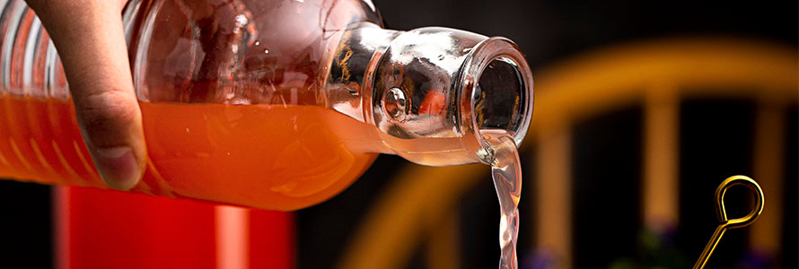 Craft orange beverage being poured from clear glass bottle