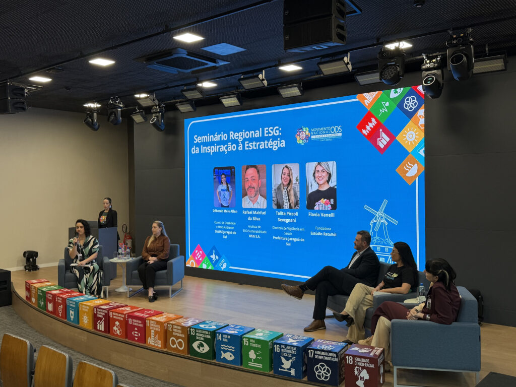 A imagem apresenta o palco do auditório da DR Aromas & Ingredientes com os painelistas do Seminário Regional ESG: Déborah Melo Aflen, coordenadora de Qualidade e Meio Ambiente do SAMAE Jaraguá do Sul; Rafael Mahfud da Silva, analista de ESG/Sustentabilidade da WEG S.A.; Talita Piccoli Sevegnani, diretora de Vigilância em Saúde da Prefeitura de Jaraguá do Sul; e Flavia Vanelli, fundadora do Estúdio RatoRói. E Maria Eduarda Grubba, analista de Sustentabilidade da DR Aromas & Ingredientes.